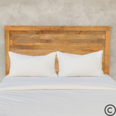 Tête de lit en manguier massif rainurée, installée derrière un lit avec draps blancs – Design naturel et élégant signé KUKUU