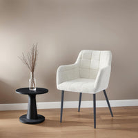 Chaise couture quadrillée avec accoudoirs et pieds en métal noir, mise en scène dans un intérieur moderne avec table d’appoint en bois – mobilier KUKUU.